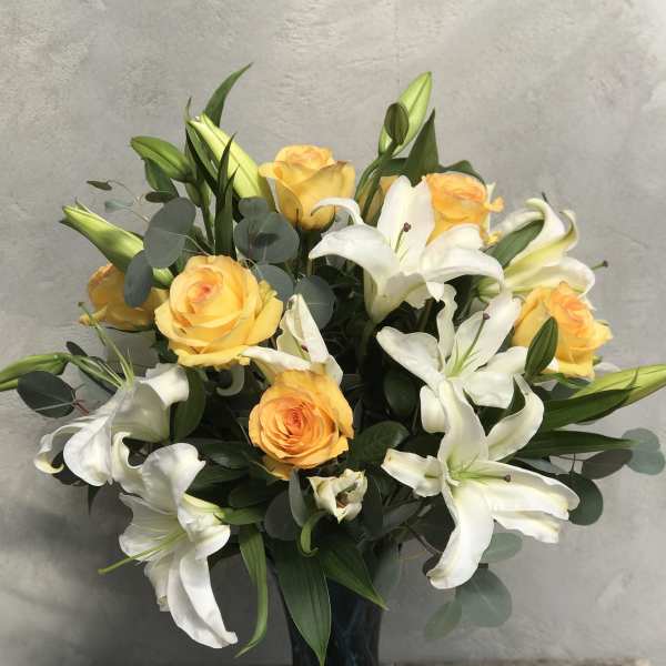 Arrangement of yellow roses and white lilies in a blue glass vase