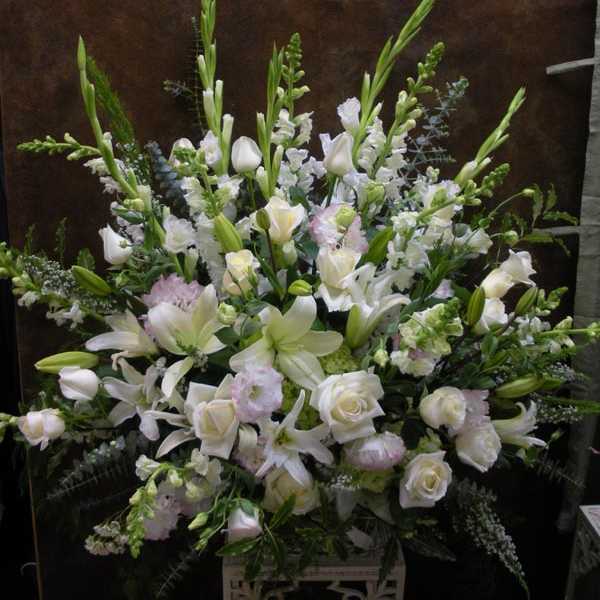 Large white floral arrangement with lilies and roses on a stand
