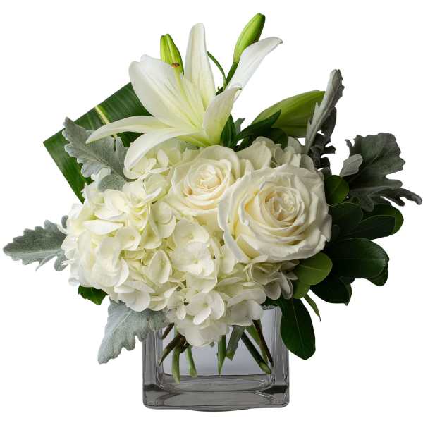 White lilies, roses, and hydrangeas arranged in a clear square vase