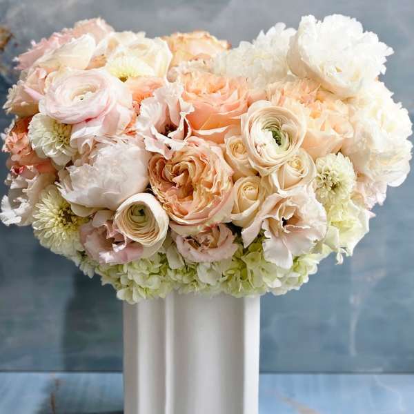 Pastel peach and white roses and ranunculus arranged in a white ceramic vase