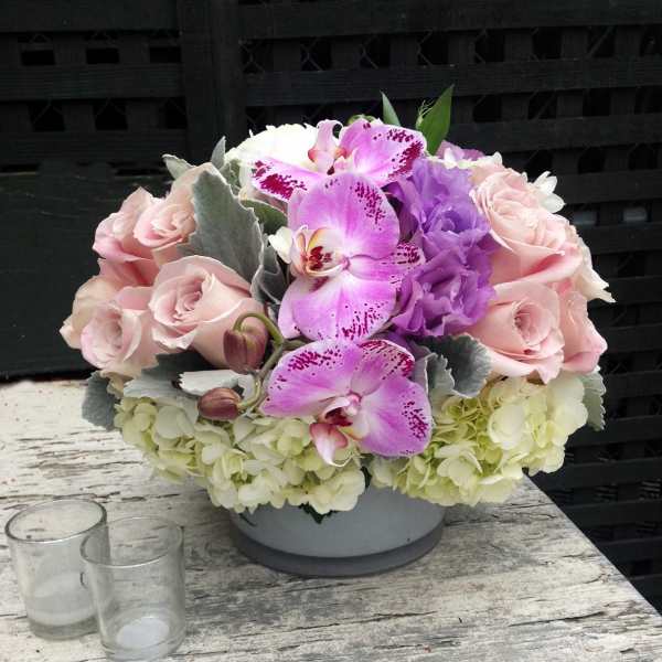 Pink roses and purple orchids arranged in a low white bowl