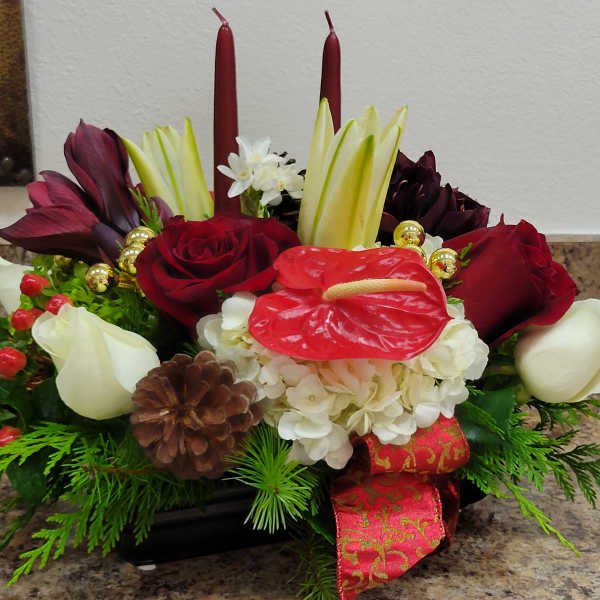 Low holiday centerpiece with red and white flowers, red anthurium, evergreens, and two dark red taper candles