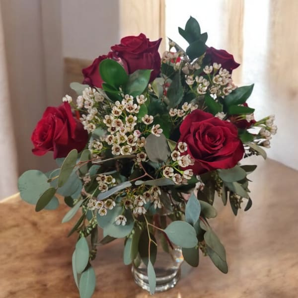 Red roses and white filler flowers in a clear glass vase