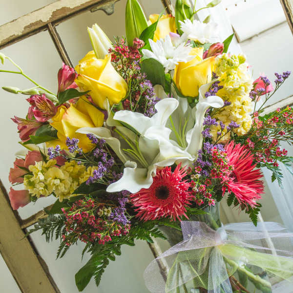 Bouquet of yellow roses, white calla lilies, and pink gerbera daisies in a glass vase