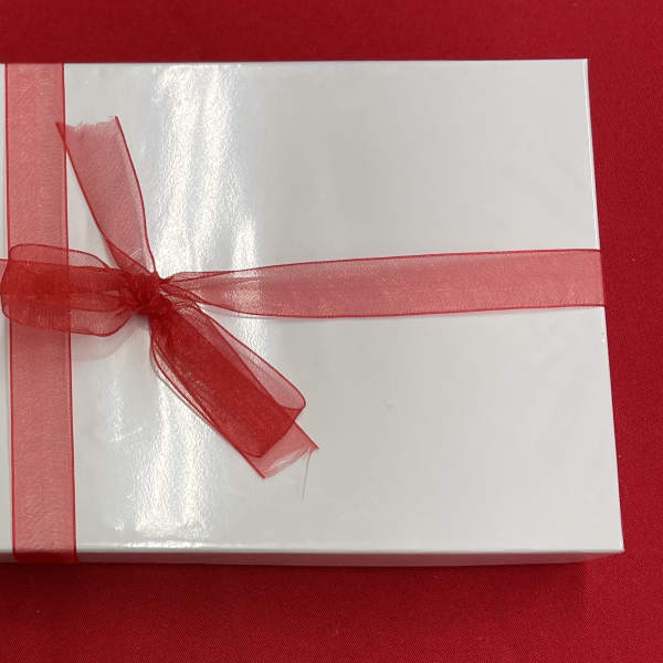 Rectangular white gift box with a sheer red ribbon and bow on a red background