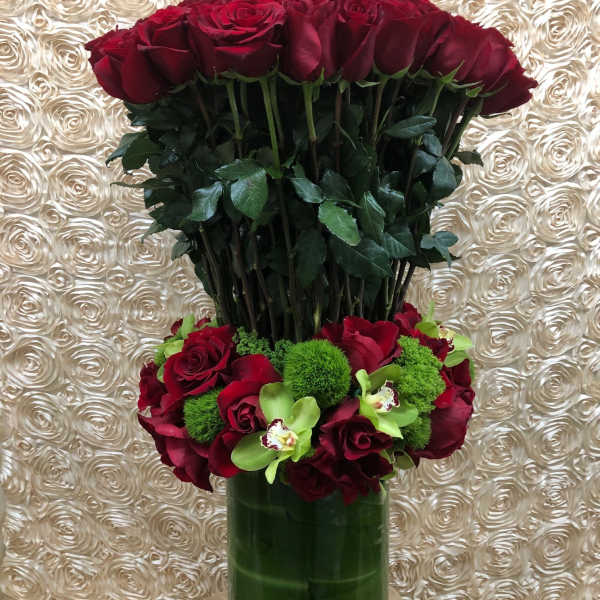 Tall arrangement of red roses in a green vase with green accents