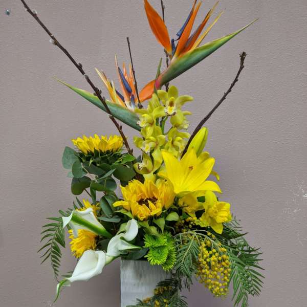 Tall floral arrangement with yellow blooms, white calla lilies, and bird of paradise in a white vase