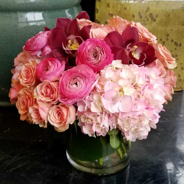 Pink and peach bouquet with roses, ranunculus, orchids, and hydrangeas in a glass vase