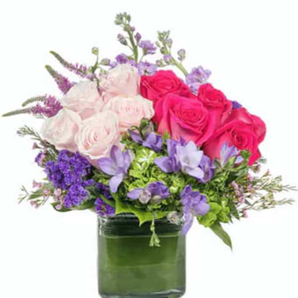 Pink and white roses with purple flowers in a green glass vase