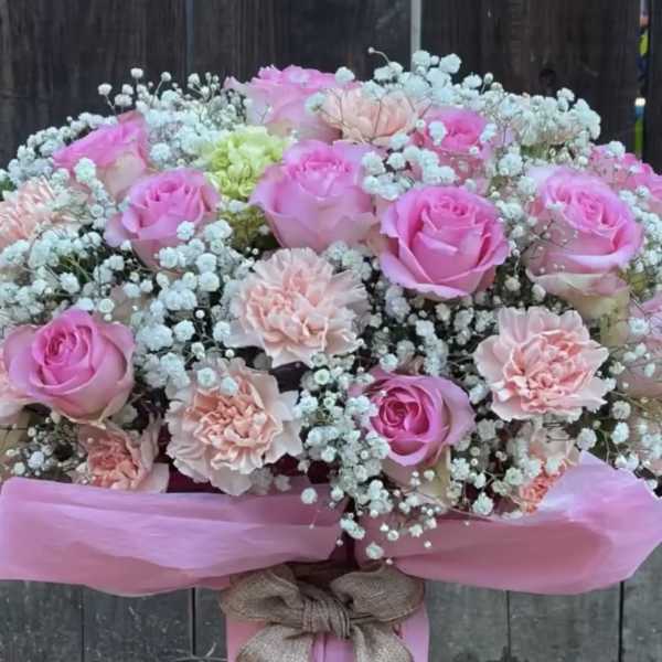 Pink roses and carnations arranged in a wrapped bouquet with baby's breath