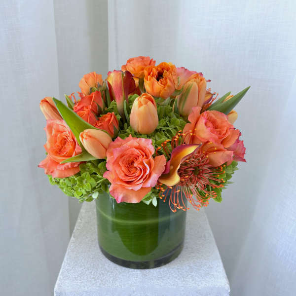Orange roses and tulips arranged in a green glass vase