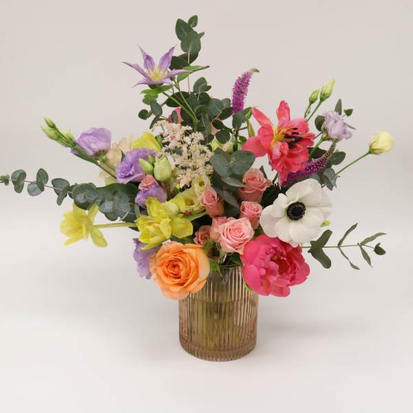 Mixed bouquet in a ribbed glass vase with pink, purple, yellow, and orange blooms