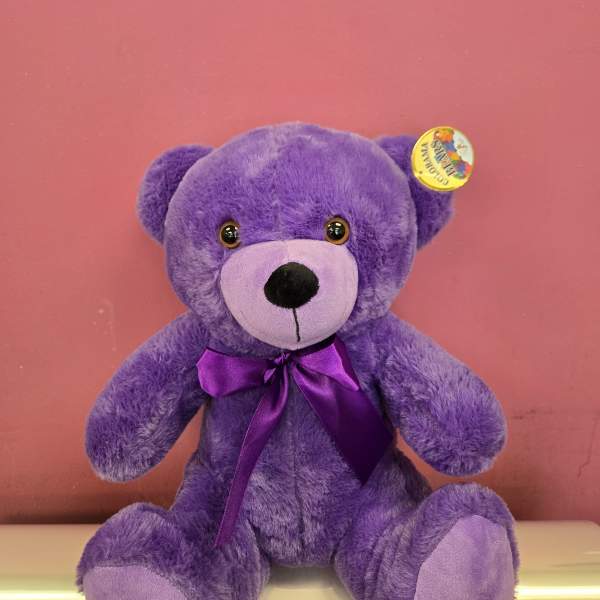 Purple teddy bear with a satin bow against a pink background