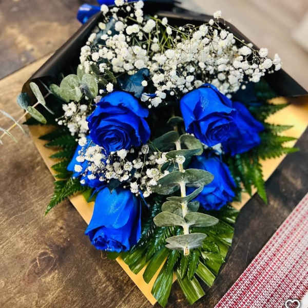 Bouquet of bright blue roses and white filler flowers wrapped in black paper with blue ribbon