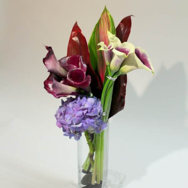Purple calla lilies and a lavender hydrangea in a clear glass vase