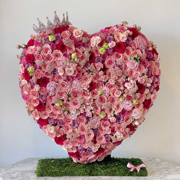 Heart-shaped arrangement of pink and red roses with a small crown on top