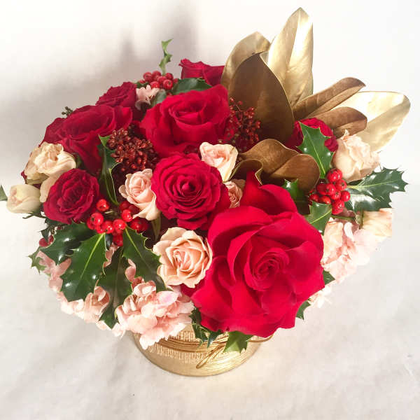 Red and blush roses arranged in a gold basket with holly leaves and berries