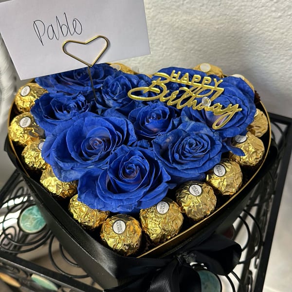 Blue roses in a heart-shaped box with gold chocolates and a birthday topper.