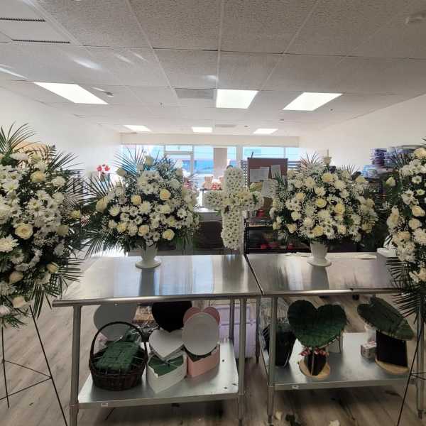White floral arrangements and a white flower cross on metal tables