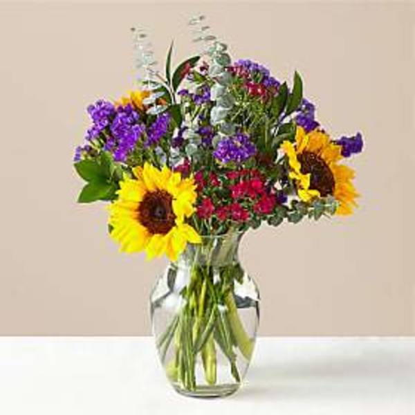 Sunflowers and purple flowers arranged in a clear glass vase