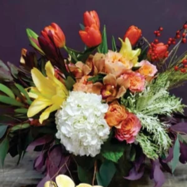 Low arrangement of orange tulips, yellow lilies, white hydrangea, and roses in a container