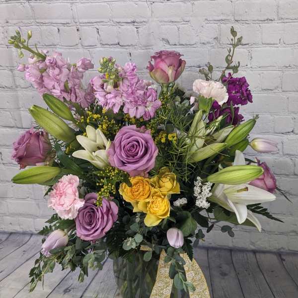 Mixed bouquet of roses, lilies, and purple blooms in a glass vase