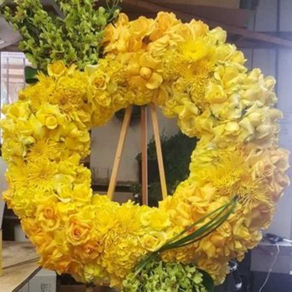 Yellow floral wreath on a wooden easel with trailing greenery