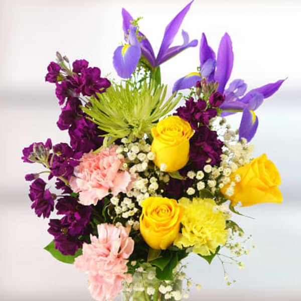 Colorful bouquet of purple, yellow, and pink flowers in a glass vase