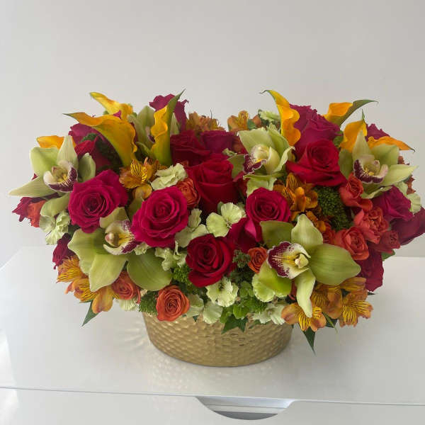Mixed bouquet of red roses, green orchids, and orange flowers in a gold bowl