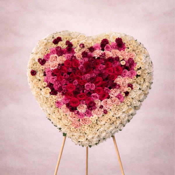 Large heart-shaped standing arrangement of red, pink, and cream roses on a wooden easel.