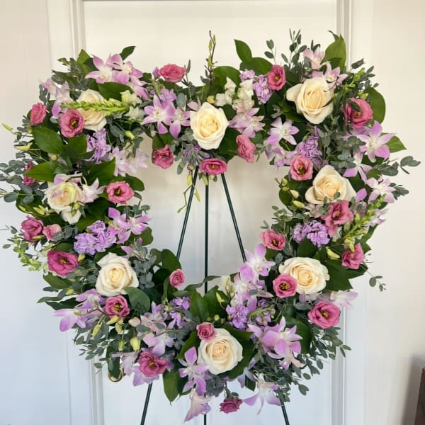 Heart-shaped floral wreath with pink, lavender, and cream blooms on a stand
