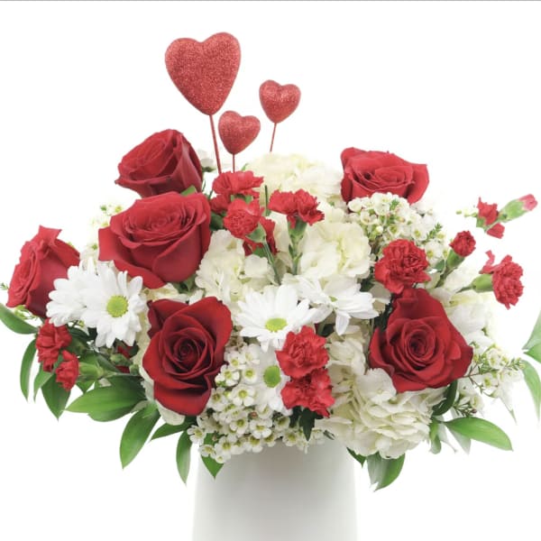 Red roses and white flowers in a white vase with heart picks