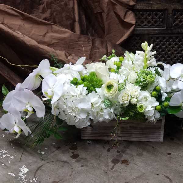 White floral arrangement with orchids and hydrangeas in a wooden box