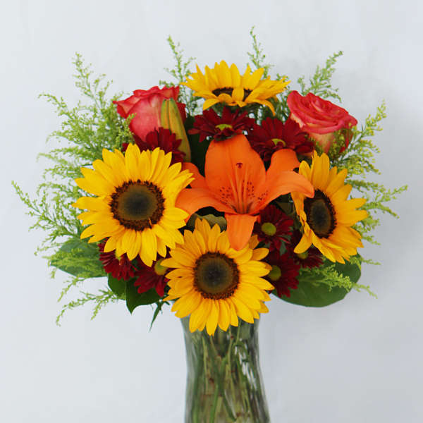 Bouquet of sunflowers, orange lilies, and red roses in a glass vase