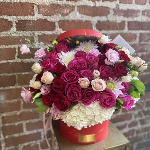 Round red hatbox filled with red and hot pink roses, blush blooms, and white hydrangeas