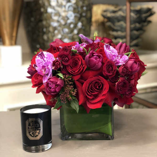 Red and pink rose bouquet in a square glass vase with a black candle beside it