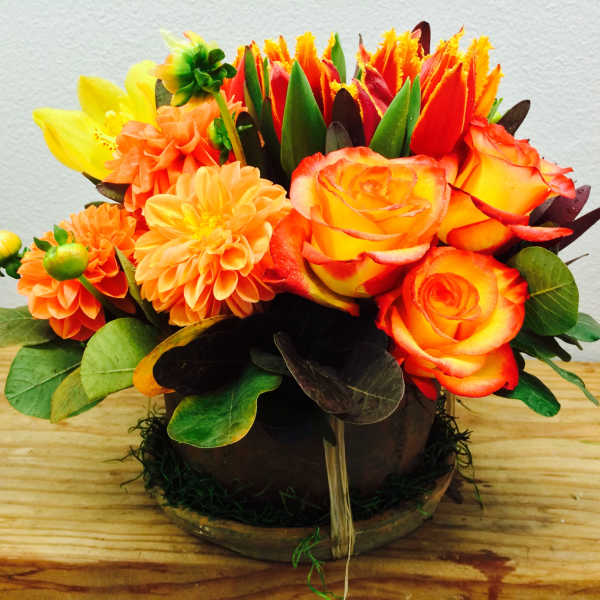 Orange and yellow floral arrangement in a low round container