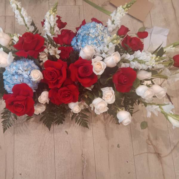 Casket spray with red and white roses, blue hydrangeas, and white lilies