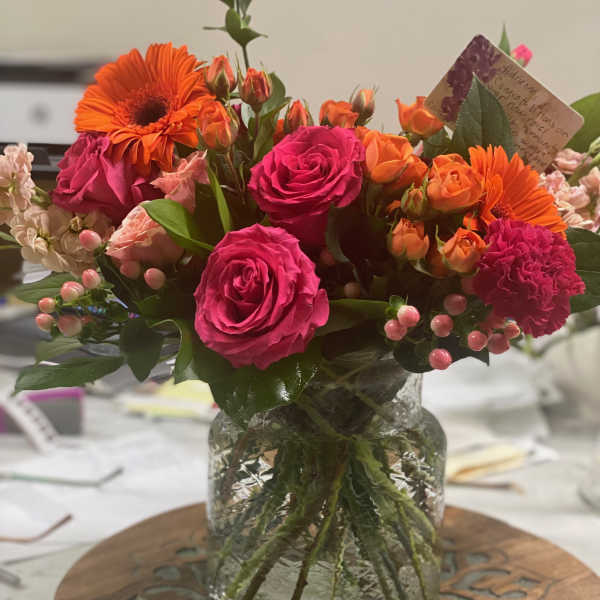 Bright mixed bouquet of pink roses and orange gerbera daisies in a glass vase