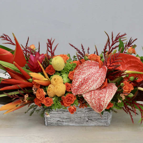 Tropical floral arrangement with orange and red blooms in a rectangular container