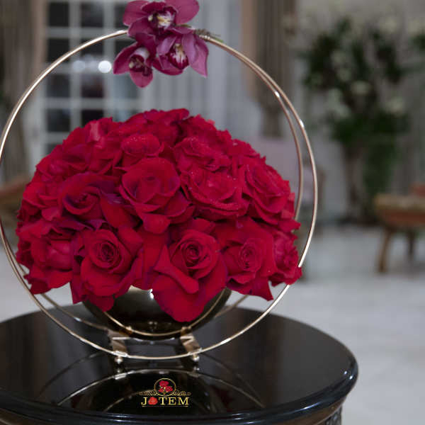 Red roses arranged in a circular metal frame on a black stand