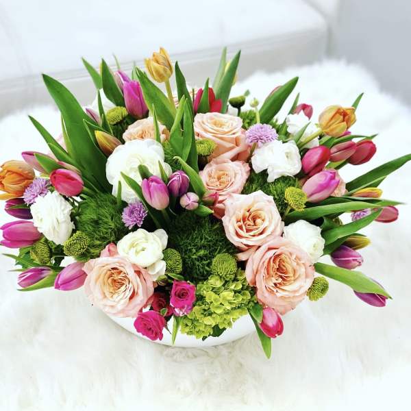 Mixed bouquet of pink, peach, white, and yellow flowers in a white container