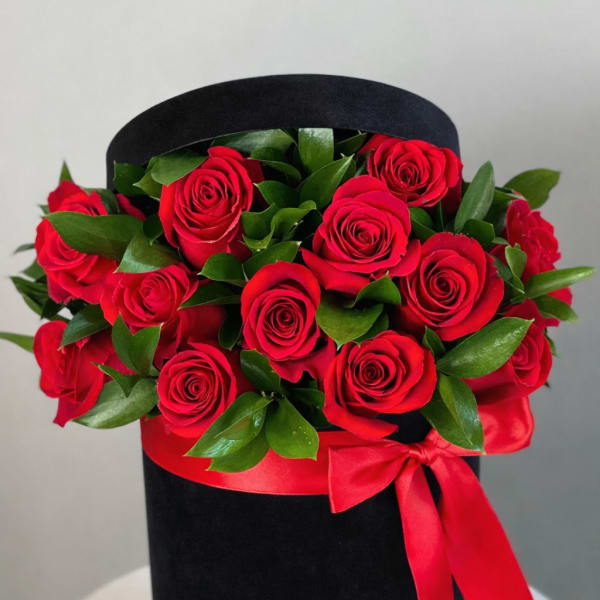 Red roses arranged in a black hat box with a red ribbon