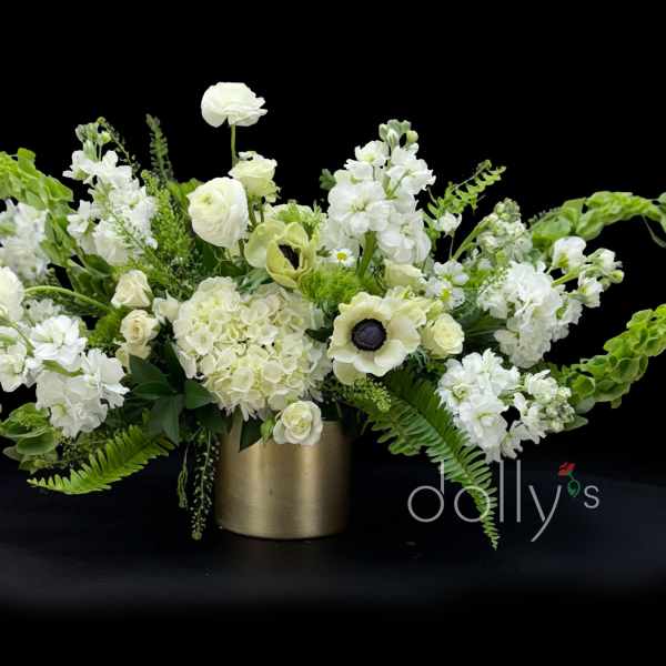 White floral arrangement in a gold vase with green accents