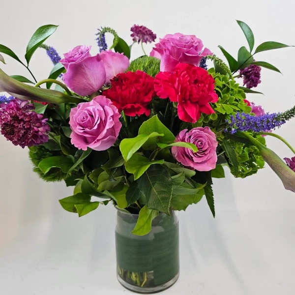 Pink roses and red carnations in a glass vase with purple accents