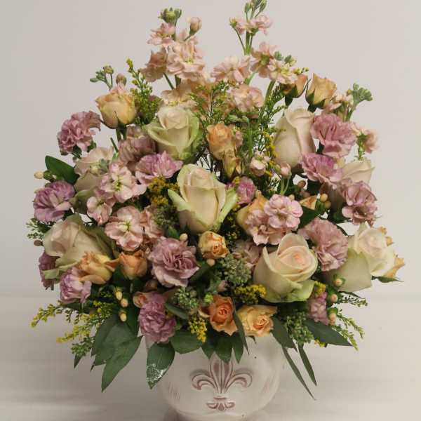 Pastel roses and mixed flowers in a white ceramic urn-style vase