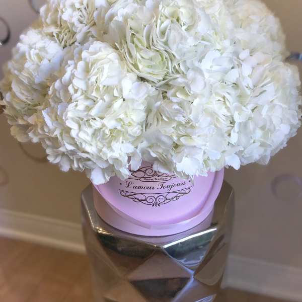 Round arrangement of white hydrangeas in a pink hat box on a metallic pedestal.