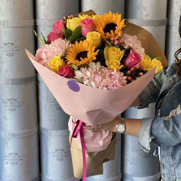 Bouquet of pink and yellow roses with sunflowers wrapped in pink paper
