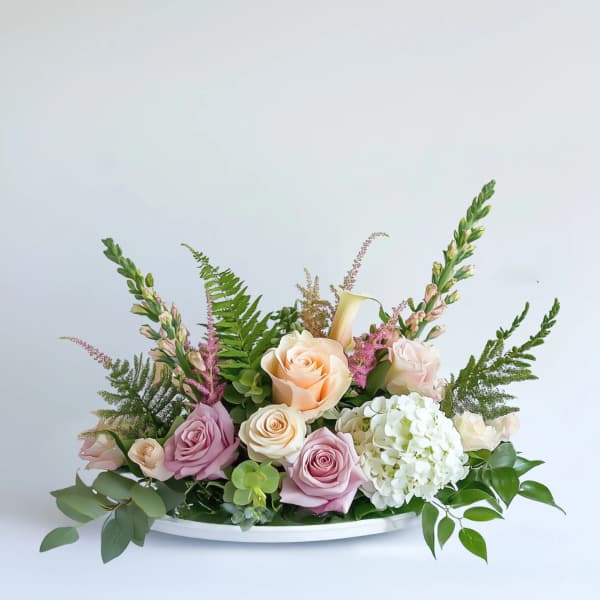 Low pastel arrangement of roses, hydrangea, calla lily, and succulents in a white oval dish