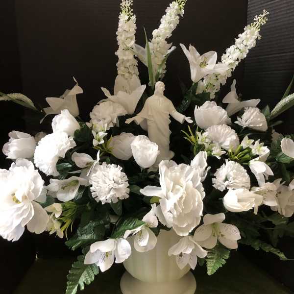 White floral arrangement with a religious statue in a pedestal vase
